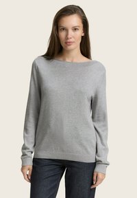Sivi pulover dugih rukava sa širokim izrezom i rebrastim manžetama, napravljen od mekanog materijala. Nosimo ga s tamnoplavim farmerkama, minimalističkog dizajna.