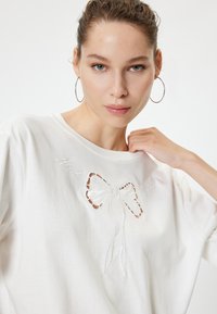 Witte katoen t-shirt met geborduurd strikontwerp en uitsnijdingen. Ontspannen pasvorm met ronde halslijn en korte mouwen.