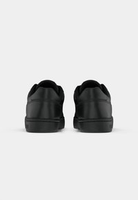 Een paar zwarte leren sneakers, van achteren gezien, met nette stiksels en een dikke zool op een witte achtergrond.