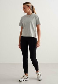 Graues Baumwoll-T-Shirt mit kurzen Ärmeln, kombiniert mit schwarzen Ripp-Leggings. Das Outfit zeichnet sich durch ein einfaches Design, eine lockere Passform und sportliche Sneaker aus.