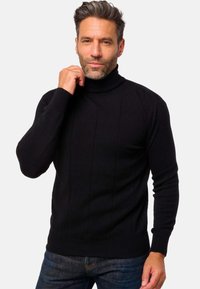 Schwarzer Rollkragenpullover mit gerippter Textur und vertikalen Nahtdetails, kombiniert mit dunklen Denim-Jeans. Einfaches, tailliertes Design.