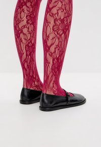 Medias de encaje magenta con patrones florales, complementadas por zapatos planos negros con una correa decorativa y un diseño de punta redondeada.