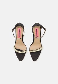 Black high-heeled sandals with an ankle strap, pointed toe, and a decorative pearl-like bead trim across the vamp. Soft textured material.
