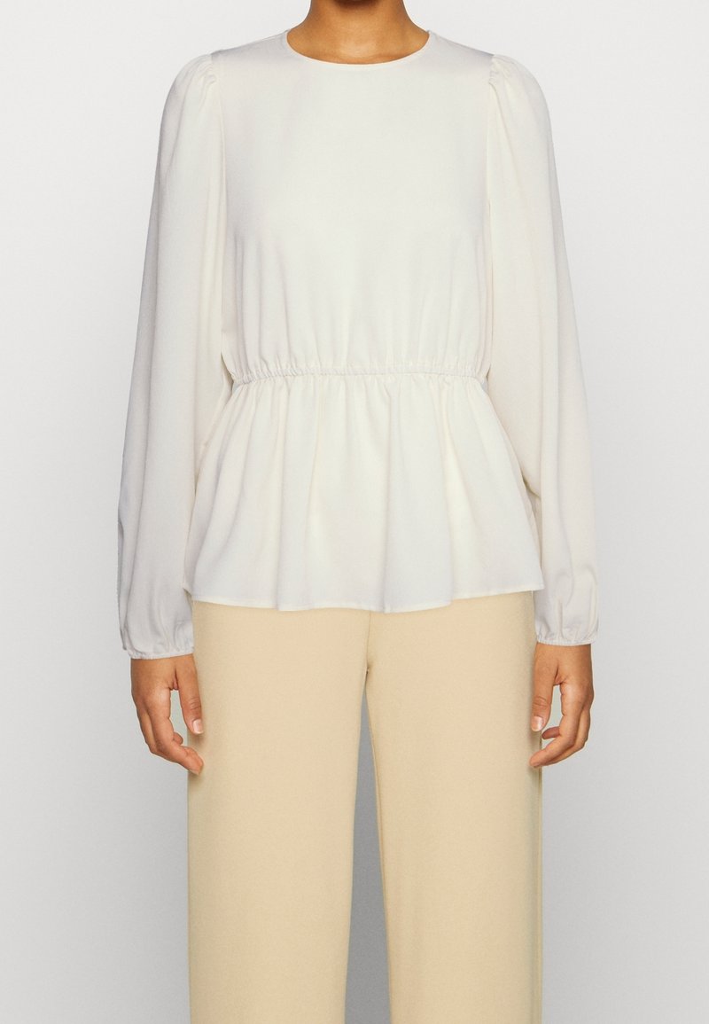 Blusa bianca a maniche lunghe con scollo rotondo, dettaglio arricciato in vita e orlo fluido. Realizzata in tessuto morbido, ha una vestibilità comoda.