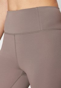 Leggings korkealla vyötäröllä hillityssä ruskeassa sävyssä. Valmistettu sileästä ja joustavasta kankaasta, jossa on tasaiset saumat ja hillitty kiilto, sisältää nykyaikaisen muotoilun.