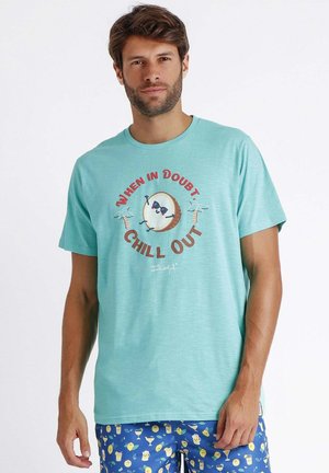 Camiseta de algodón color azul verdoso con un gráfico redondo que muestra palmeras y un logo. El texto dice "CUANDO HAYA DUDA, RELÁJATE". Mangas cortas, corte relajado.