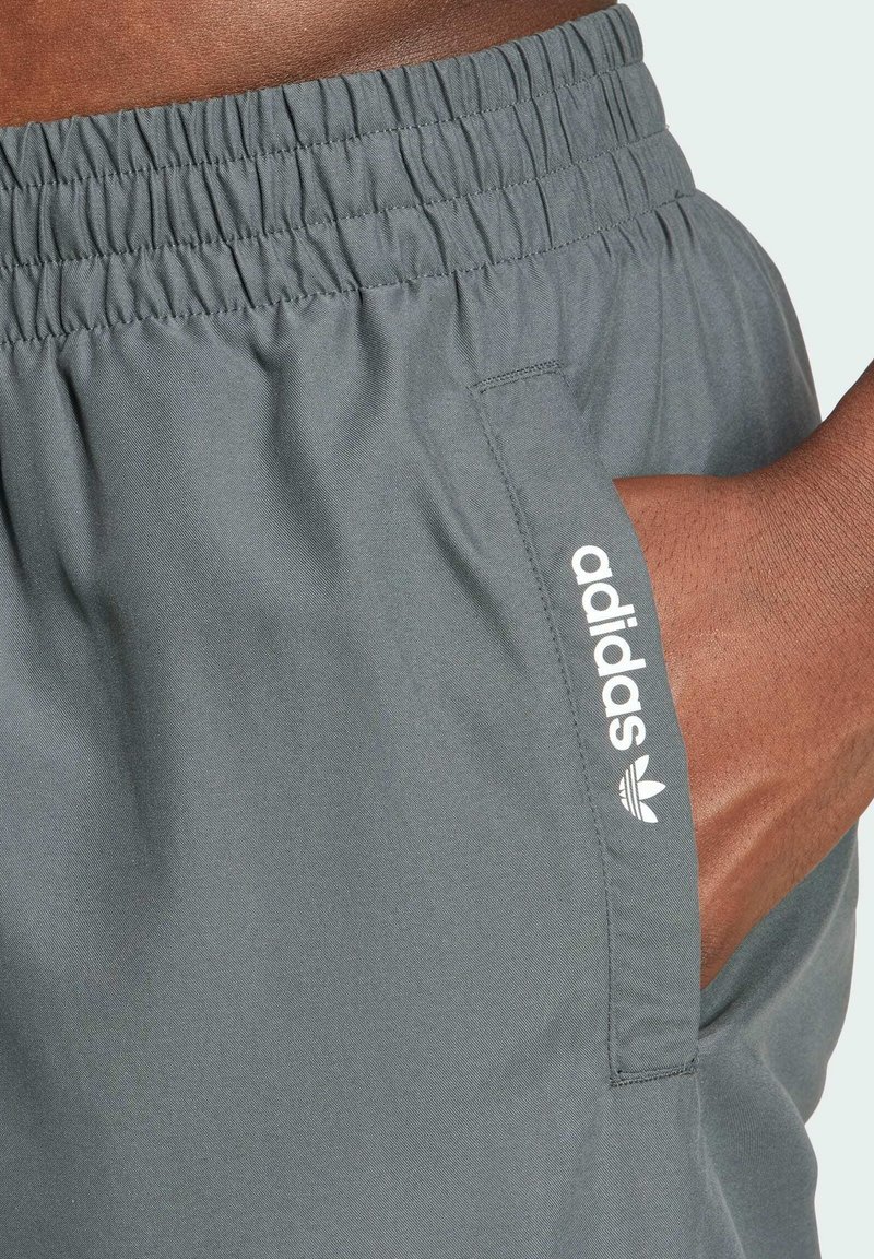 Mørkegrå shorts med elastisk talje og sidelomme; har et hvidt Adidas-logo vist på venstre side. Glat, letvægtsstof.