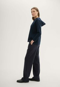 Felpa blu navy con cappuccio, tessuto alveolato e vestibilità rilassata abbinata a pantaloni larghi scuri. Entrambi i capi presentano tasche.