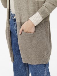 Svetlohnedý pletený cardigan s prednou vreckom, nosený cez rebrovaný krémový top a skombinovaný s vysokými modrými džínsami. Mäkká textúra, voľný strih.