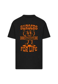 Melna T-krekli ar oranžu karikatūras hamburgeru, kuram ir brilles, roku paceltās, un teksts "BURGERI VISAI DZIVI" zem tā treknā, stilizētā fontā.