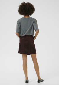 T-shirt gris surdimensionné à manches courtes, associé à une jupe en velours côtelé bordeaux. Chaussures noires à enfiler avec des clous en argent. Design simple, coupe décontractée.