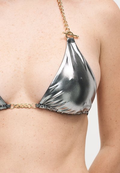 Κοντινό πλάνο ενός ατόμου που φοράει ασημί μεταλλικό τοπ μπικίνι με χρυσλές αλυσίδες στο στράπες και κούμπωμα μπροστά.