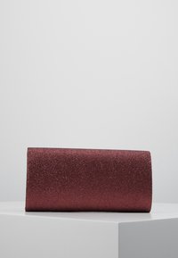 Błyszcząca bordowa kopertówka o prostokątnym kształcie, gładkiej fakturze i bez widocznych elementów metalowych. Umieszczona na minimalistycznej białej powierzchni.