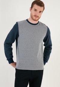 Felpa grigia a fantasia con maniche blu navy. Presenta un collo tondo e polsini a coste, realizzata in morbido cotone misto con una texture piacevole.