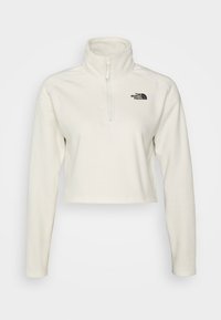 Sudadera de forro polar blanca con cuello con cremallera. Presenta mangas largas y un logo negro en el lado izquierdo del pecho. Diseño corto. Textura suave.