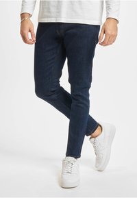 Mørkeblå denimjeans med smal passform, med oransje sømmer, kombinert med hvite joggesko.