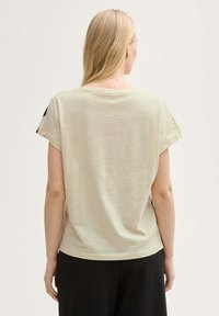 Lichtbeige T-shirt met korte mouwen, een losse pasvorm, ronde halslijn en een gladde textuur. Zwarte accenten op de mouwen zorgen voor visuele interessen.