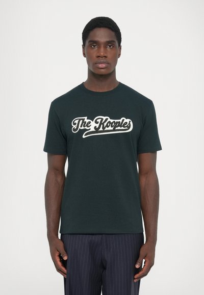 Camiseta de algodón negra con un logo blanco "The Kooples" en una fuente cursiva, mangas cortas y un diseño clásico de cuello redondo.