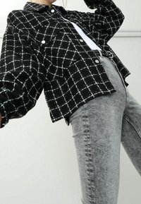 Svart- och vitrutig jacka med puffärmar, knäppt fram och två bröstfickor, kombinerad med ljusgrå figurnära jeans.