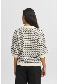 Stickad krämfärgad tröja med ett strukturerat vågmönster i marinblått. Puffärmar och ribbad nederkant fulländar designen.