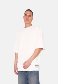 Hvid, oversized t-shirt lavet af bomuld, med rund halsudskæring og korte ærmer. Inkluderer et logotag nederst til venstre på kanten.