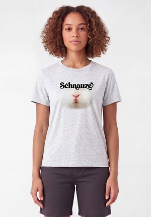 Vrouw met krullend haar die een lichtgrijs T-shirt draagt met de tekst "Schnauze" en een close-up van de neus van een konijn op de voorkant gedrukt.