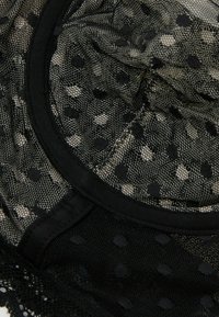 Zwart gaasstof met stippenpatroon, voorzien van elastische rand en kantaccenten langs de randen. Gestructureerd en semi-doorzichtig.