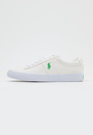 Biały niski sneaker z białymi sznurówkami, zielonym haftowanym logo gracza polo z boku i białą gumową podeszwą.