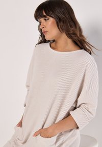 Lichtbeige geribde trui met een brede halslijn, lange mouwen en voorzakken, met een loose fit en een zachte textuur.