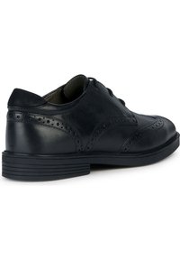 Svart läderskor med brogue-dekor, rundad tå, snörning och låg gummisula. Slät textur med en slipad yta.
