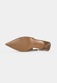 Chaussure à talon haut marron à bout pointu vue depuis la semelle, montrant une petite surface texturée antidérapante et un logo doré près de la voûte plantaire.