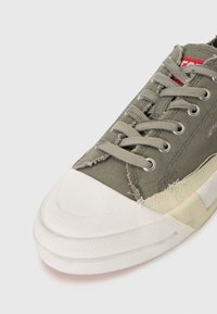 Baskets en toile vertes avec un embout en caoutchouc blanc, des lacets gris et des bords effilochés visibles. Comprend des œillets en métal et une semelle texturée.
