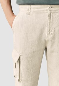 Pantalones cargo de lino beige con un corte relajado, que cuentan con cierre de botón, bolsillos laterales y una textura sutil.