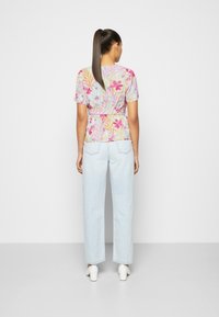 Blouse florale à manches courtes, présentant des motifs roses et orange sur un fond clair, associée à un jean large bleu clair et des talons blancs.