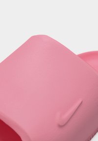 Κοντινό πλάνο ενός ροζ σανδαλιού Nike slide που δείχνει το υφασμένο λουράκι με το ανάγλυφο λογότυπο Nike swoosh.