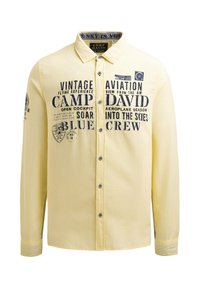 Gelbes Langarmhemd mit schwarzem Drucktext und Grafiken, Knopfleiste vorne, klassischer Kragen und kontrastierenden Nähten.