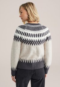 Sweter z wełny dzianej z jasnoszarym korpusem, ciemnoszarymi akcentami oraz geometrycznymi wzorami na yoke i dolnej części. Tekstura ryżowa.