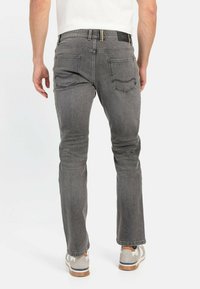 Dark gray jeans featuring a slim fit, five-pocket design, stitched accents, and a branded waistband, paired with light gray sneakers.