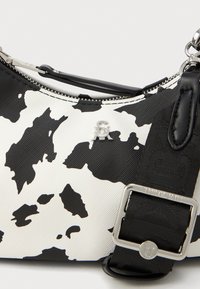 Bolso bandolera con estampado de vaca, superficie texturizada, herrajes de plata y una correa negra ajustable con detalle de hebilla.