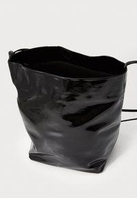 Bolso de piel negra tipo bucket con un acabado brillante, textura ligeramente arrugada, parte superior abierta y tirantes delgados. Sin detalles de herrajes visibles.