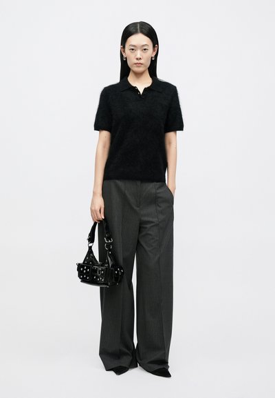 Μαύρο χνουδωτό πόλο πουκάμισο με κοντά μανίκια, σε συνδυασμό με γκρι παντελόνι ευρείας γραμμής με ρίγες. Κρατώντας μια μικρή μαύρη δερμάτινη τσάντα με μεταλλικές λεπτομέρειες.