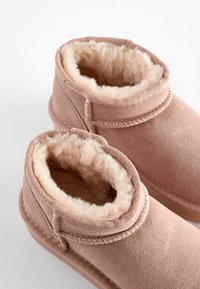 Rosa ankelstövlar med en mjuk, pälsfodrad insida och slät yta. Har sydda detaljer och en rundad form.