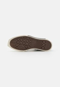 Suela de zapato de goma marrón con un patrón geométrico y bordes en crema. Texturada para agarre, con una parte delantera plana y un tacón redondeado.