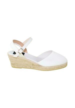 Sandalia tipo espadrille blanca con cuña, puntera cerrada, correa en el tobillo y suela de yute trenzado sobre fondo blanco.