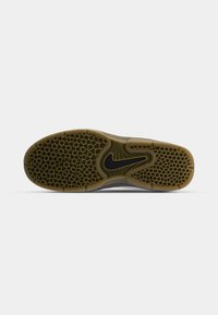 Semelle de chaussure avec motif en nid d'abeille et logo Nike noir central sur une base en caoutchouc marron sur fond blanc.
