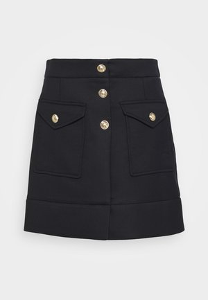 Jupe noire trapèze avec boutons dorés à l'avant, deux poches à rabat avec détails de boutons dorés et un large ourlet.