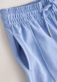 Pantaloni cu talie elastică albastru deschis, cu șnur și buzunar lateral deschis, din material texturat, prezentați întinși pe o suprafață deschisă.