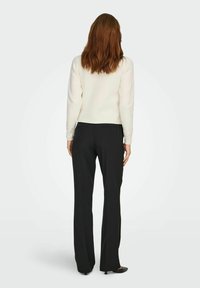 Maglione bianco con maniche decorate, abbinato a pantaloni neri attillati. L'outfit è minimalista con texture lisce e una silhouette aderente.