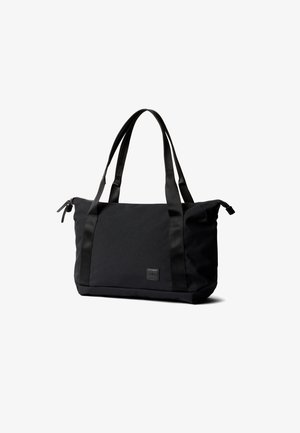 Borsa tote rettangolare nera con doppie maniglie lunghe, chiusura superiore con cerniera e piccola toppa con logo frontale, posata su sfondo bianco.