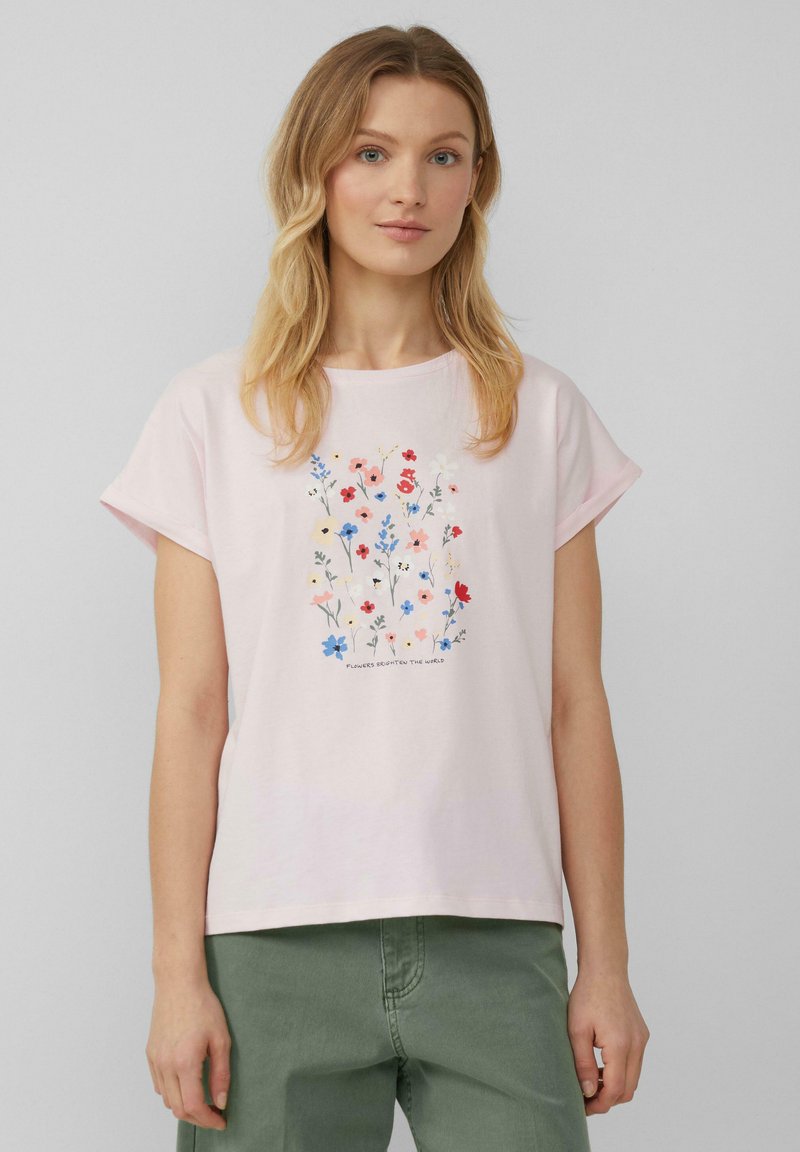 T-shirt rose clair à manches courtes, ornée d'un motif floral dans diverses couleurs, avec le texte "Les fleurs changent le monde" en dessous du motif.